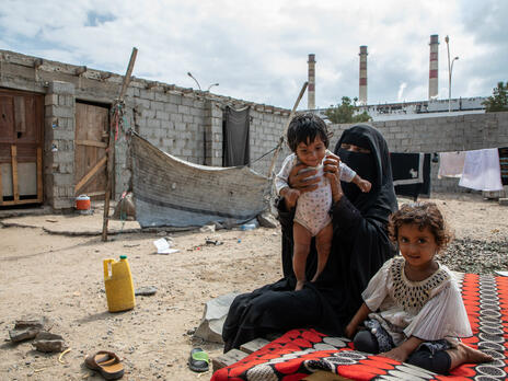 A mother and her two young children seated outdoors in Yemen