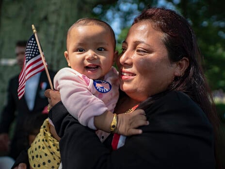 A woman holds a baby and an American flag at a naturalization ceremony