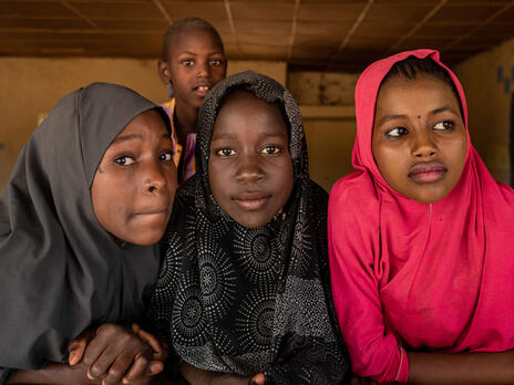 Three adolescent girls at a school in northeastern Nigera lean on the windowsill of their classroom as another girl stands behind them.
