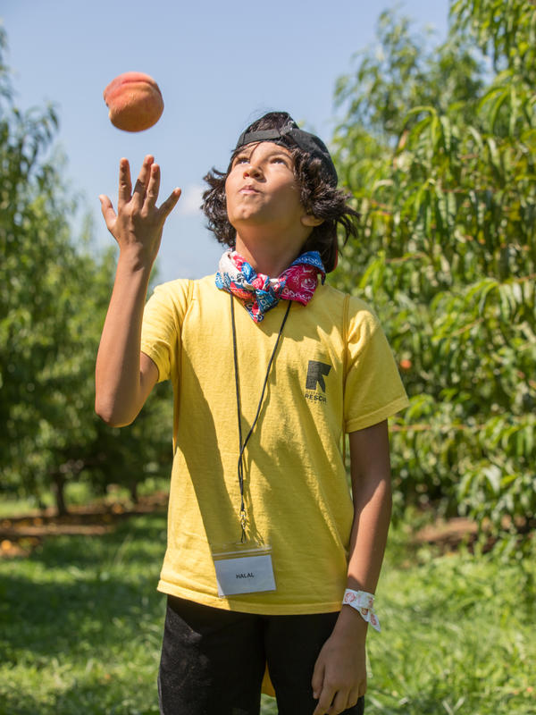 RYSA student enjoying peach picking. RYSA student wearing a cap and a RYSA shirt, enjoying peach picking and throwing it in the air.