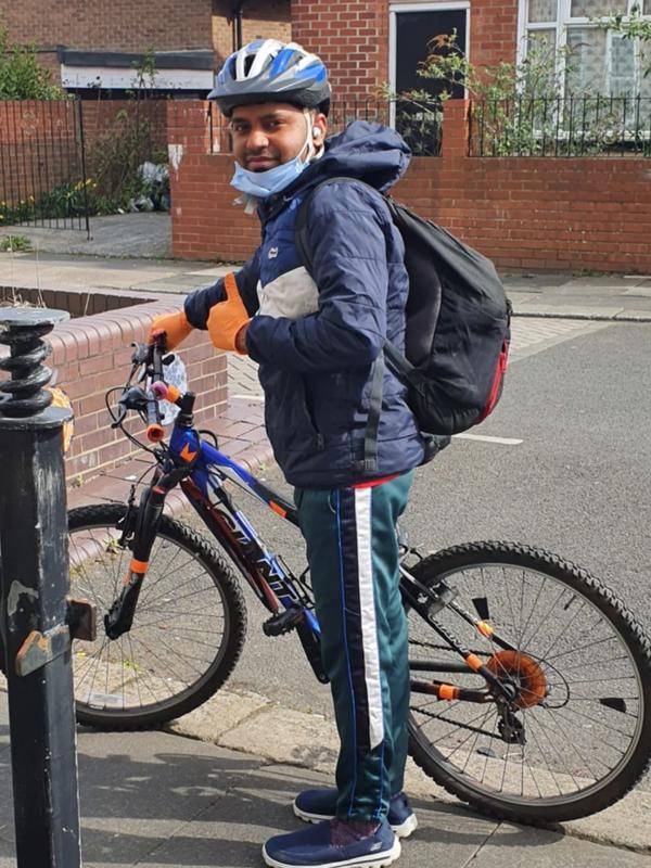 Md Mominul Hamid Md Mominul Hamid stands next to his bike and gives a thumbs up. He is wearing a blue helmet and orange gloves and a black backpack.
