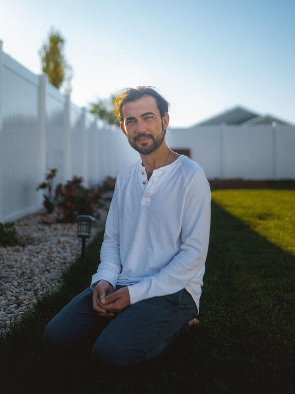 Shadi in his backyard Shadi, wearing a white botton-down shirt, sits in his backyard in front of his white fence near his garden.