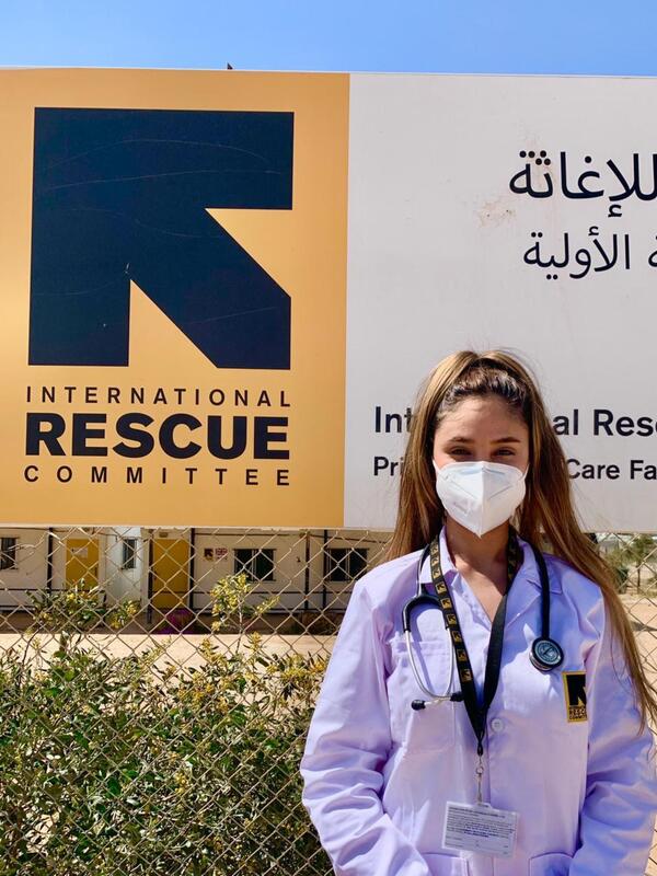 Dr. Rose Al-Nsour, a medical doctor for the IRC in Jordan Wearing a mask, Dr. Rose Al-Nsour stands outside in front of an IRC logo.