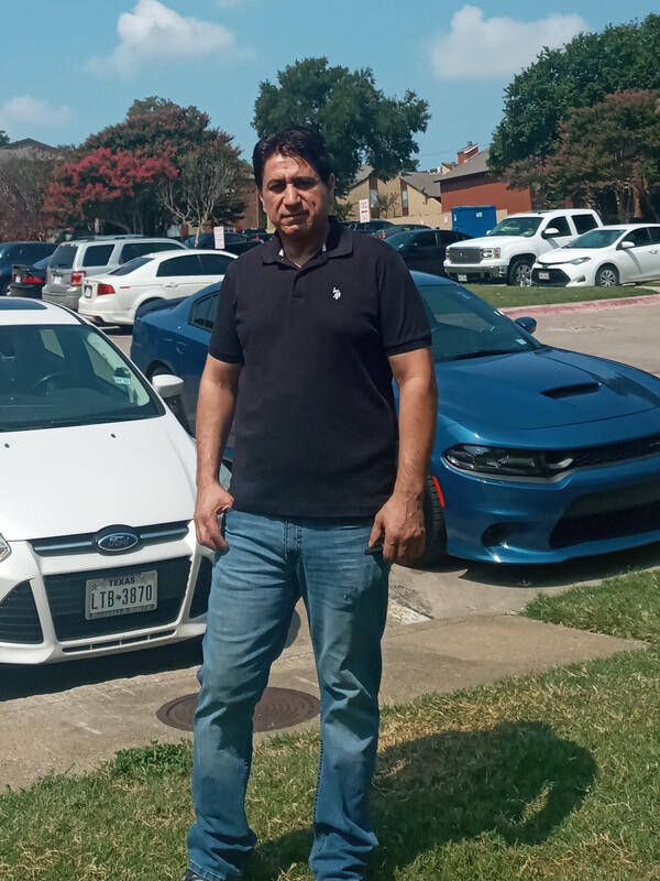 Ehsanullah stands in front of a parking lot and apartment complex 