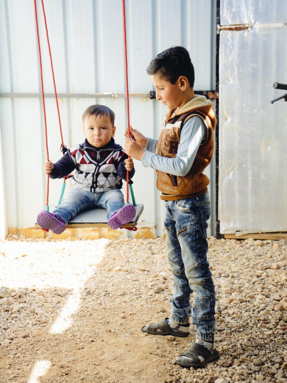 In einem Flüchtlingslager wird ein kleiner Junge von seinem großen Bruder beim Schaukeln angeschubst.