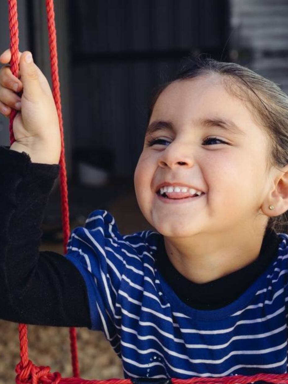 Ein fünfjähriges Mädchen mit Hirntumor sitzt auf einer Schaukel und lacht