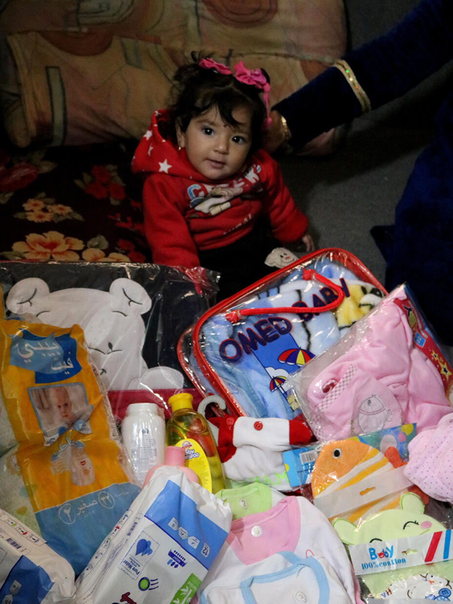 Baby im Areesha Flüchtlingslager sitzt zwischen dem Inhalt des Neugeborenen Pakets
