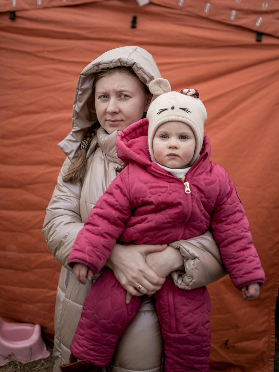 Iryna hält ihr Kind im Arm während beide in die Kamera schauen und Winterbekleideung tragen 