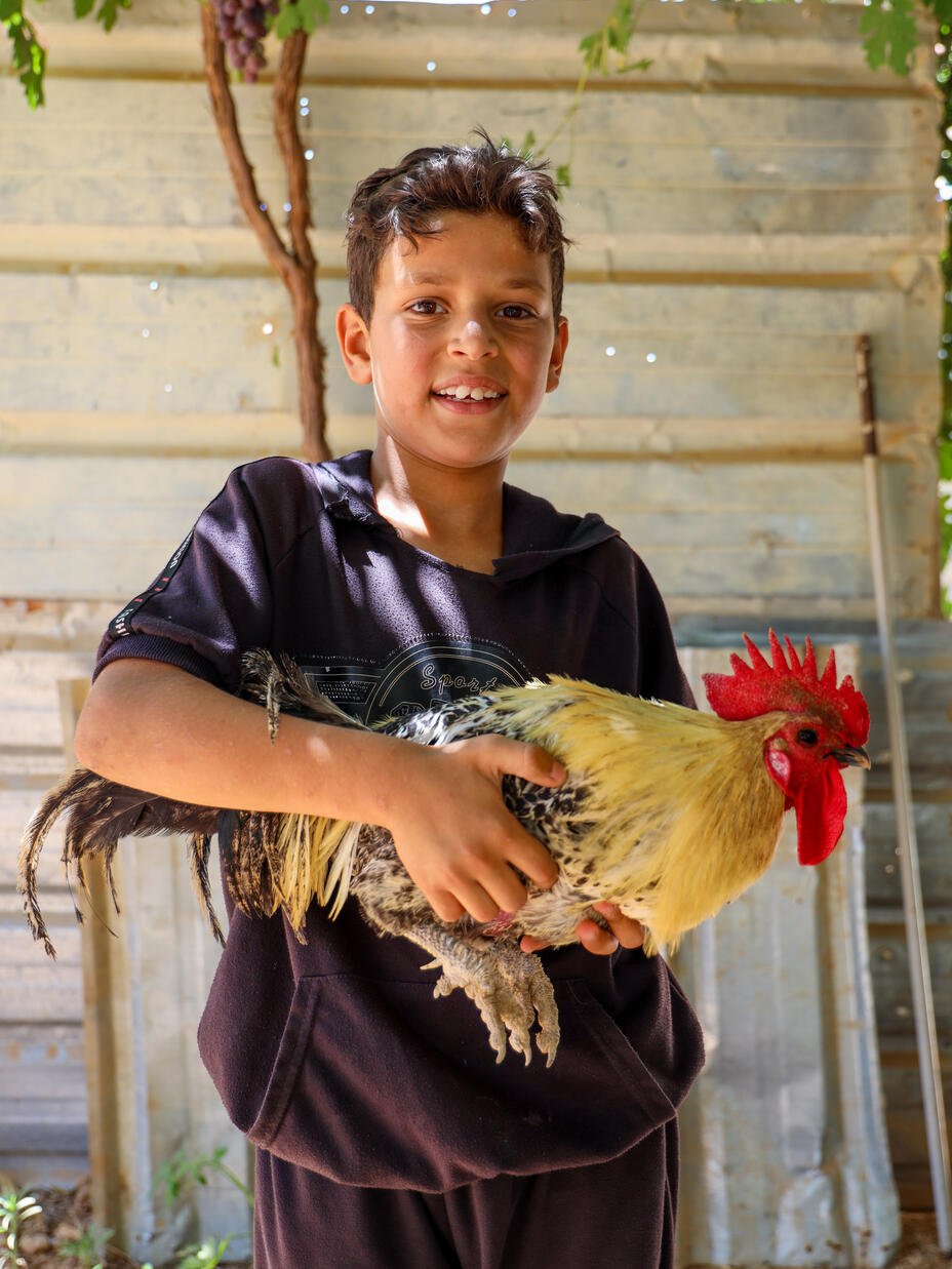 Nawras smiles and stands holding his pet rooster