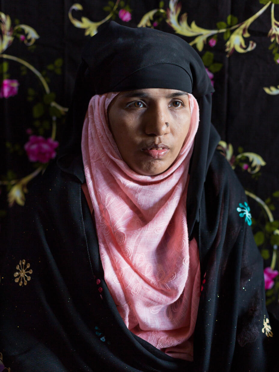 Portrait of Tahera Begum in front of a colourful background, looking to the right