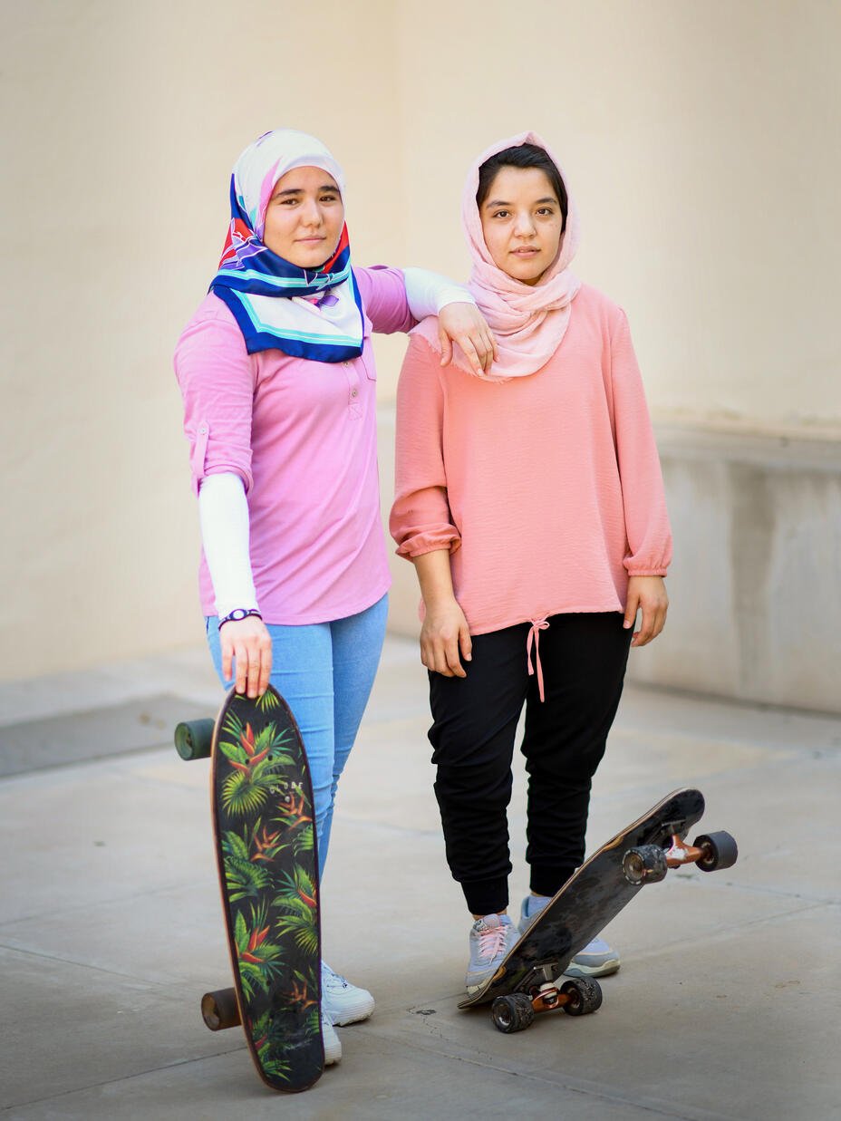 Arifa and Hadisa stand next to one another with their skateboards. 