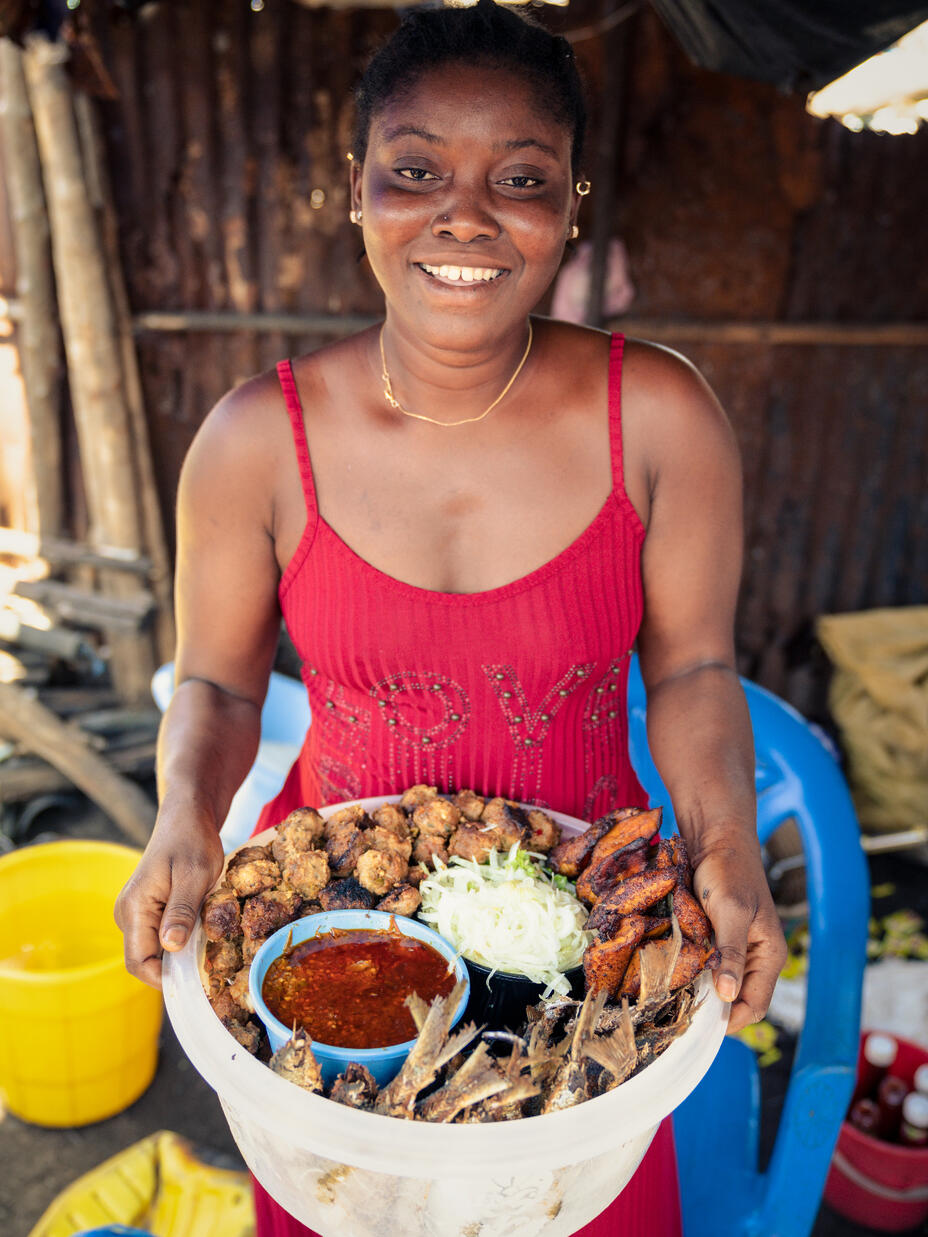 Wara stands smiling holding food from her business.