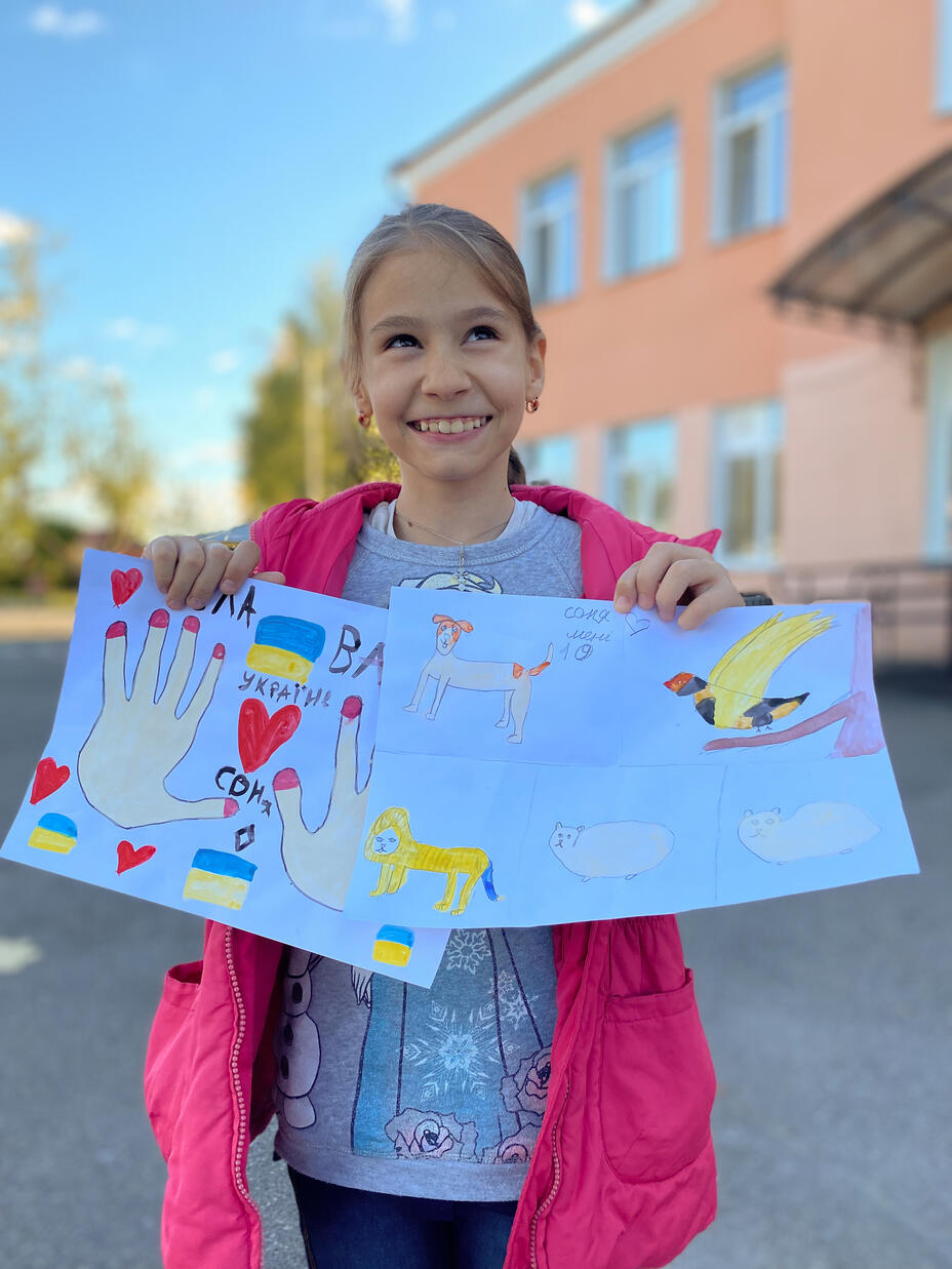 Safiya holds up artwork to the camera, smiling.