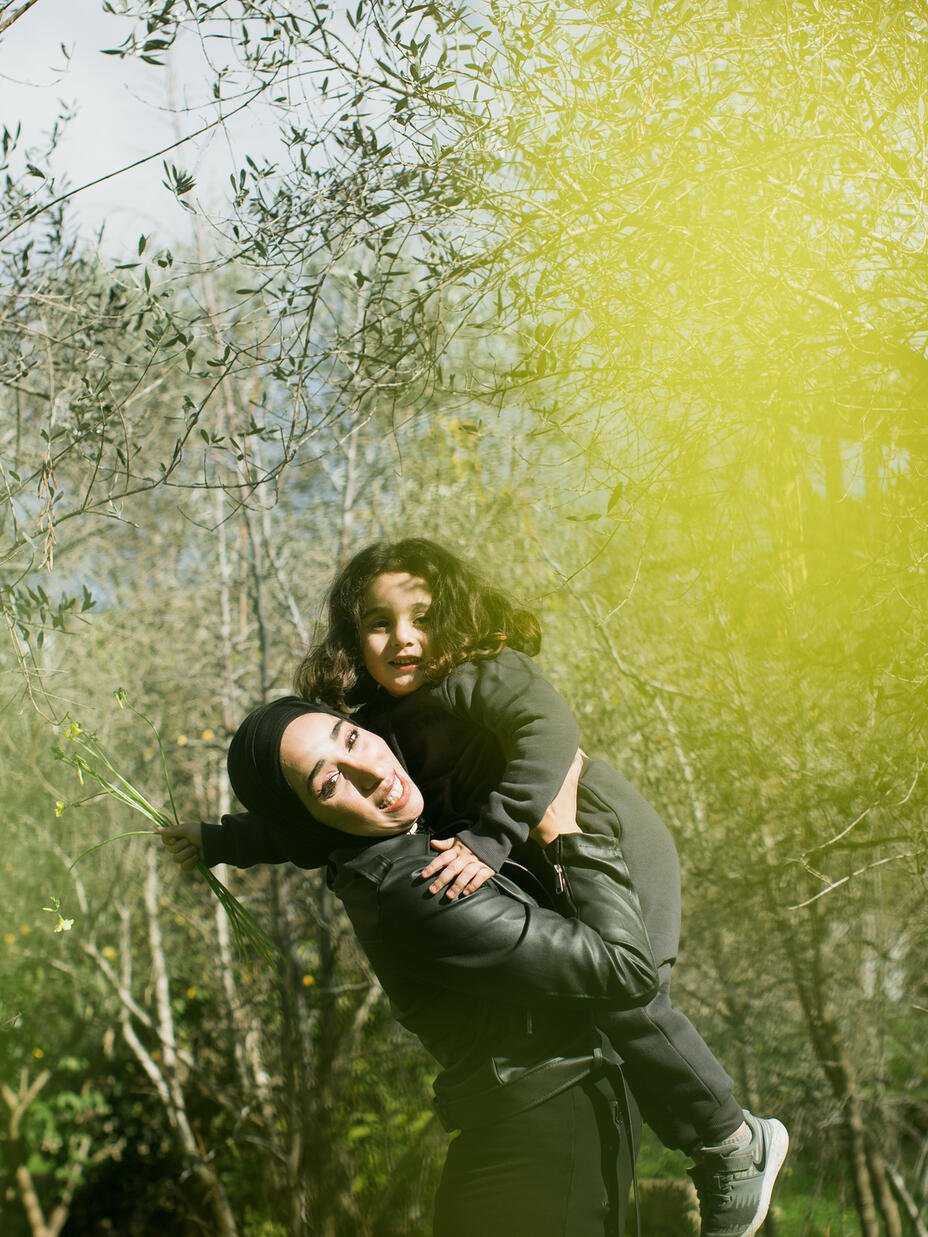 Nour holds her younger brother, Youssef, up in the air, surrounded by trees.