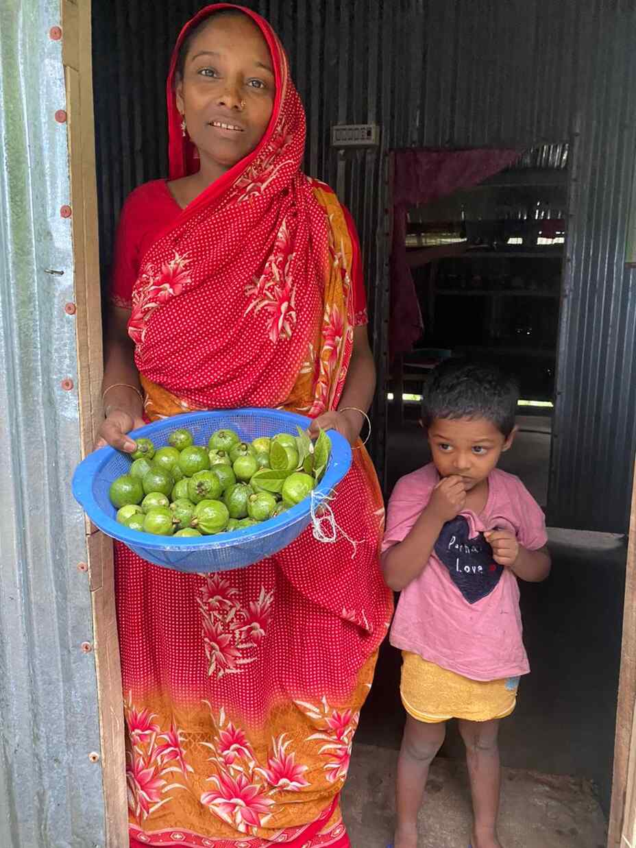 I en region vid kusten i Bangladesh, poserar Nehar för ett foto vid utgången till ett hus. Bredvid henne står ett litet barn.