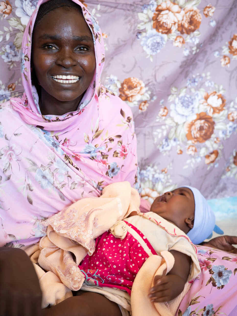 Smiling woman wearing pink head scarf holding child