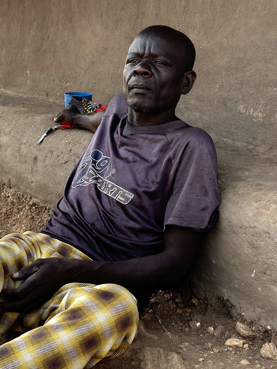 James Taban sitter mot en husvägg. Hans dotter är en av många unga mammor i Uganda.