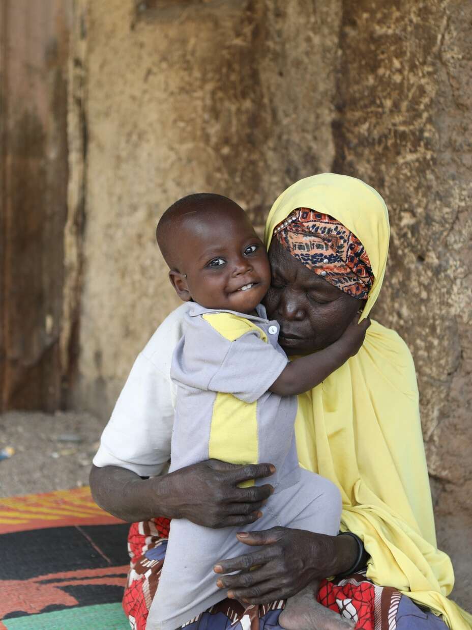 A grandmother holds her grandson, who received malnutrition treatment from the IRC, outside their home in Nigeria.