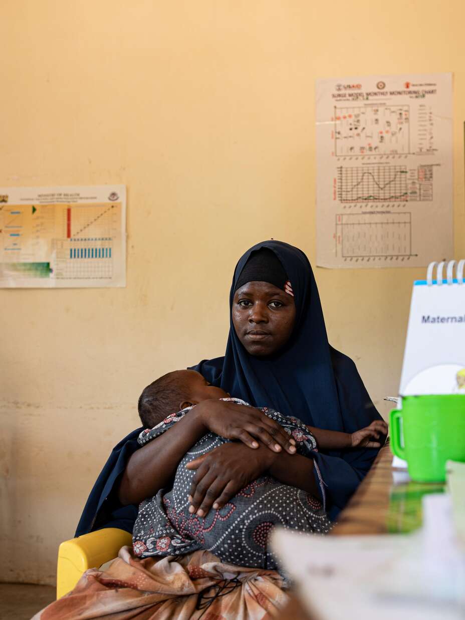 Shukri with her child on her laps, looking at the camera.