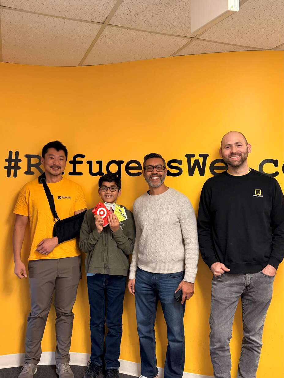 A group of individuals stand in front of a yellow background. In the center, a student holds gift cards.