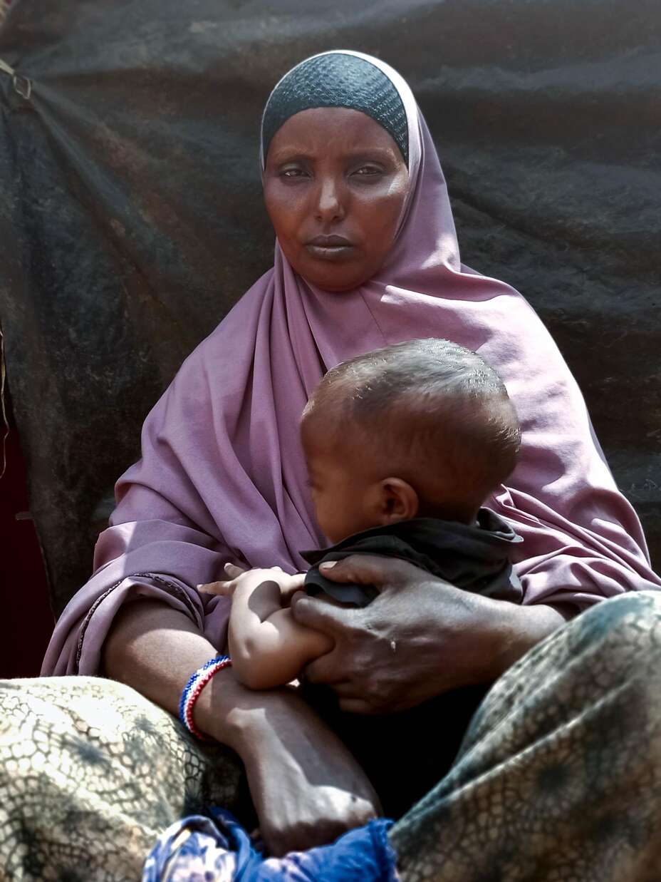 Alima, 33, sits on a low wooden stool outside the shelter she recently built from the materials provided through the IRC's EU-funded work.