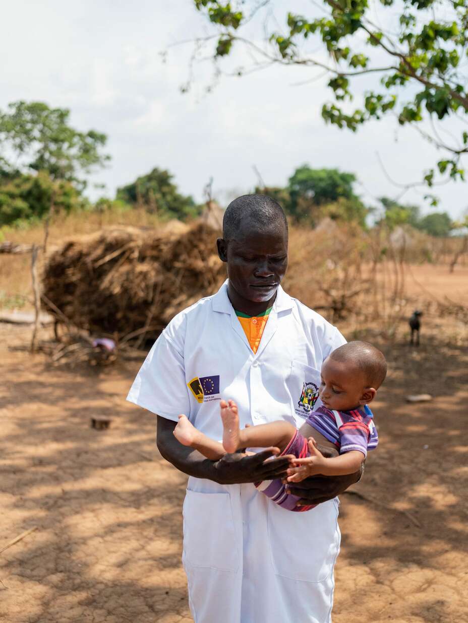 An IRC health worker holding a child during one of the routine visits to the village.
