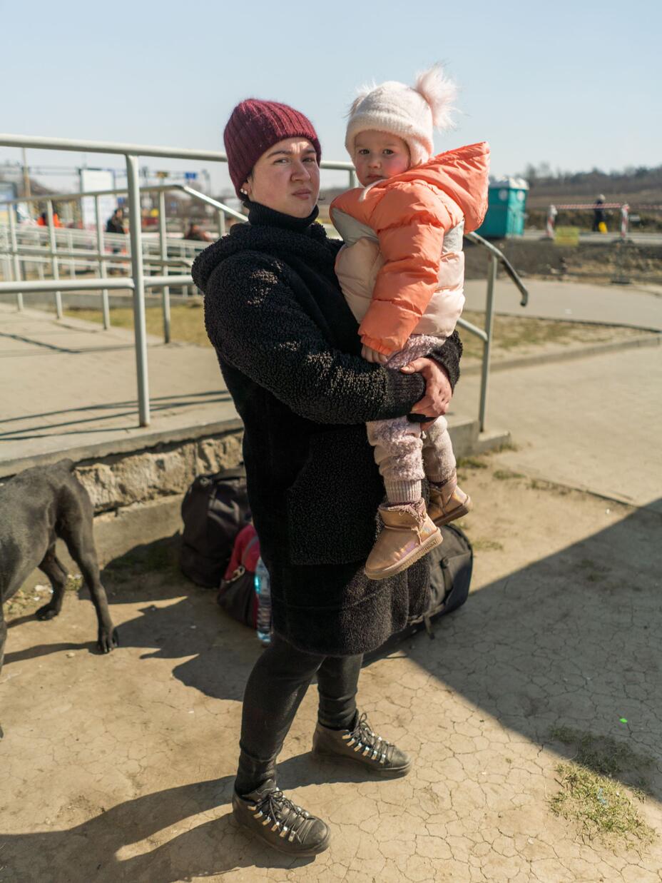 A woman holding her child and standing next to a dog.