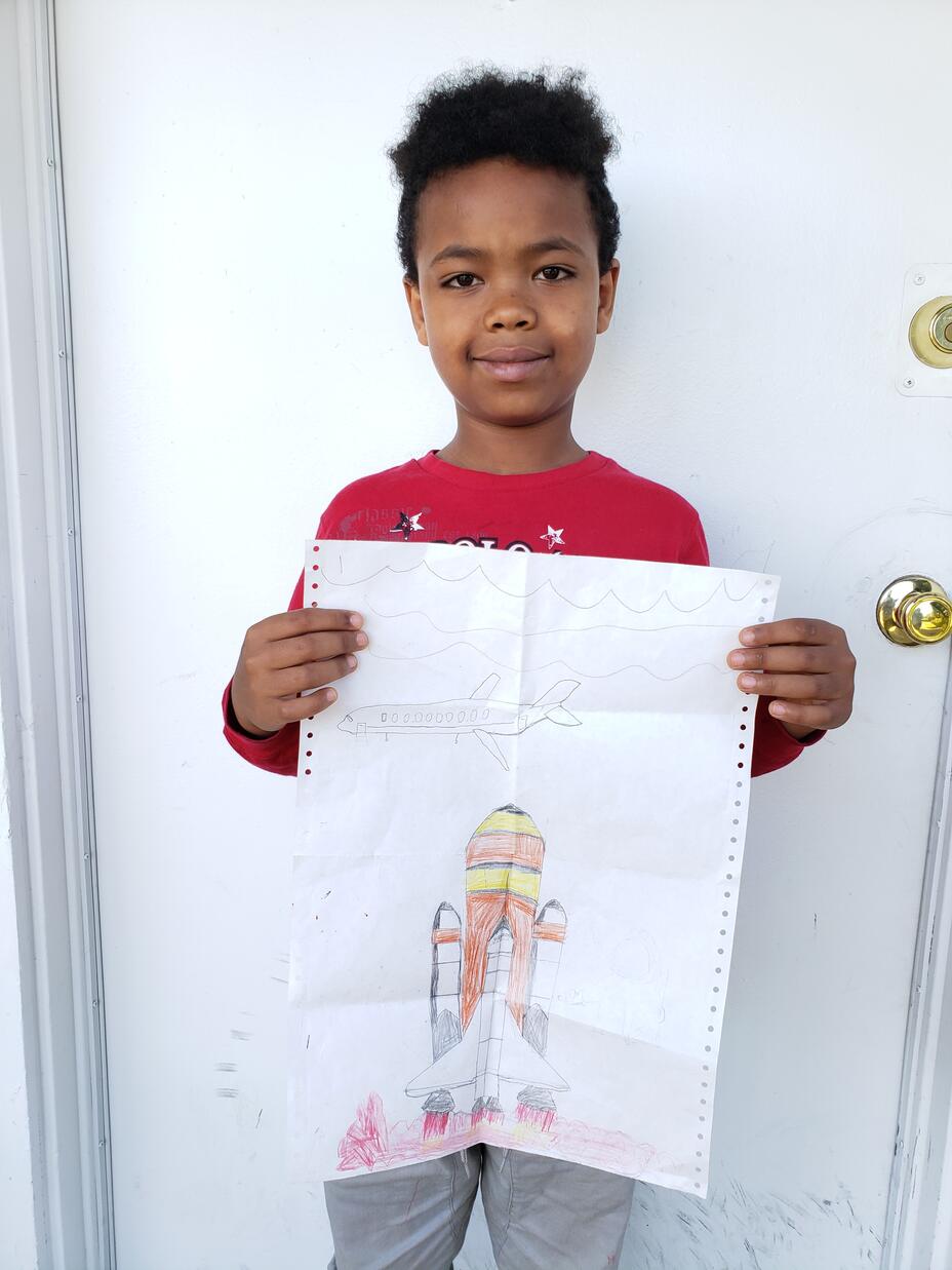 Kudus, a 5-year-old boy from Eritrea, stands outside his new home in Seattle holding his picture of a space shuttle rocket launch.