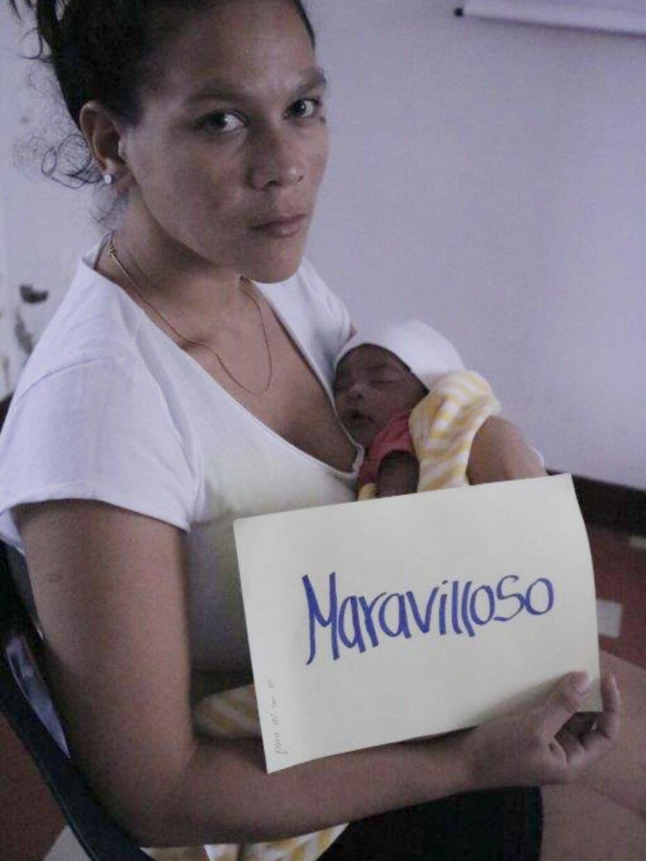 Verónica Andrade, a Venezuelan migrant in Colombia and a new mother, holds a sign saying “Maravilloso” (or “Wonderful”) along with her new baby while looking at the camera. 