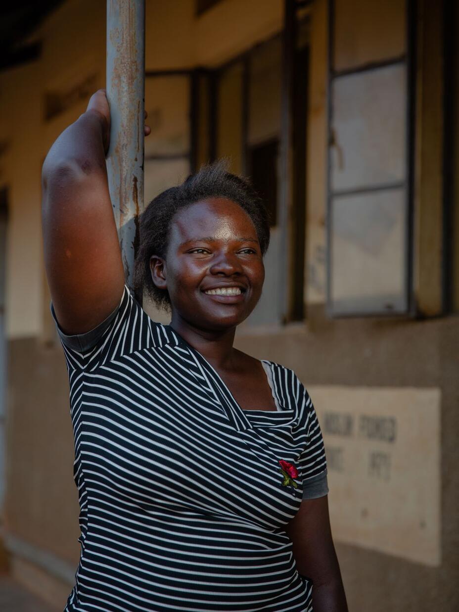 Jackie leans against a pole outside, smiling. 