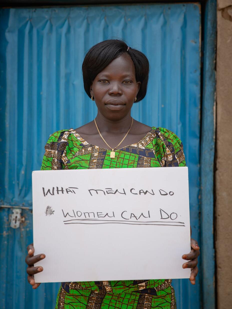 Foni holds a sign that says "What men can do, women can do." 