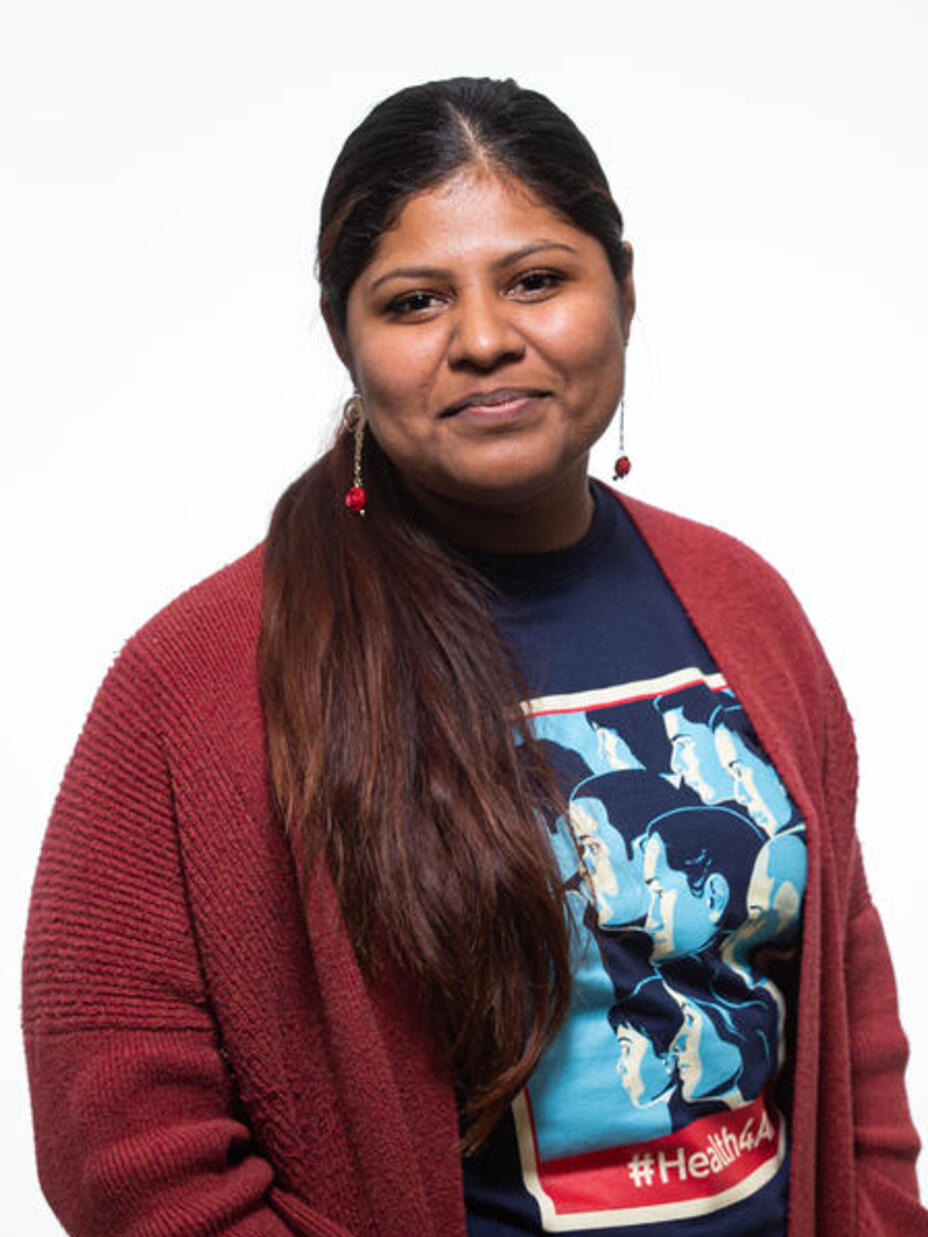 Lupe smiles and looks at the camera while wearing a blue shirt that says #Health4All and a red cardigan. 