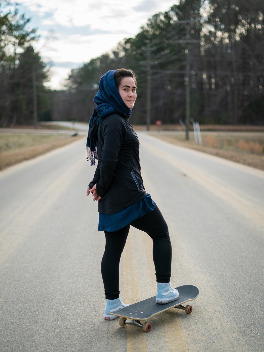 A young woman on a skateboard on the road looks at the camera
