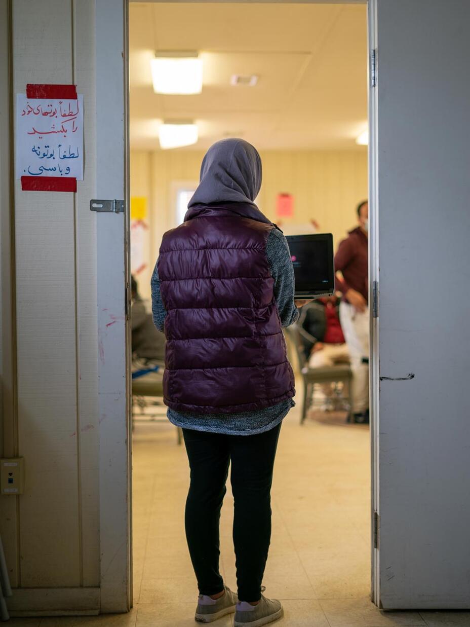 A young woman stands in a doorway holding a laptop.