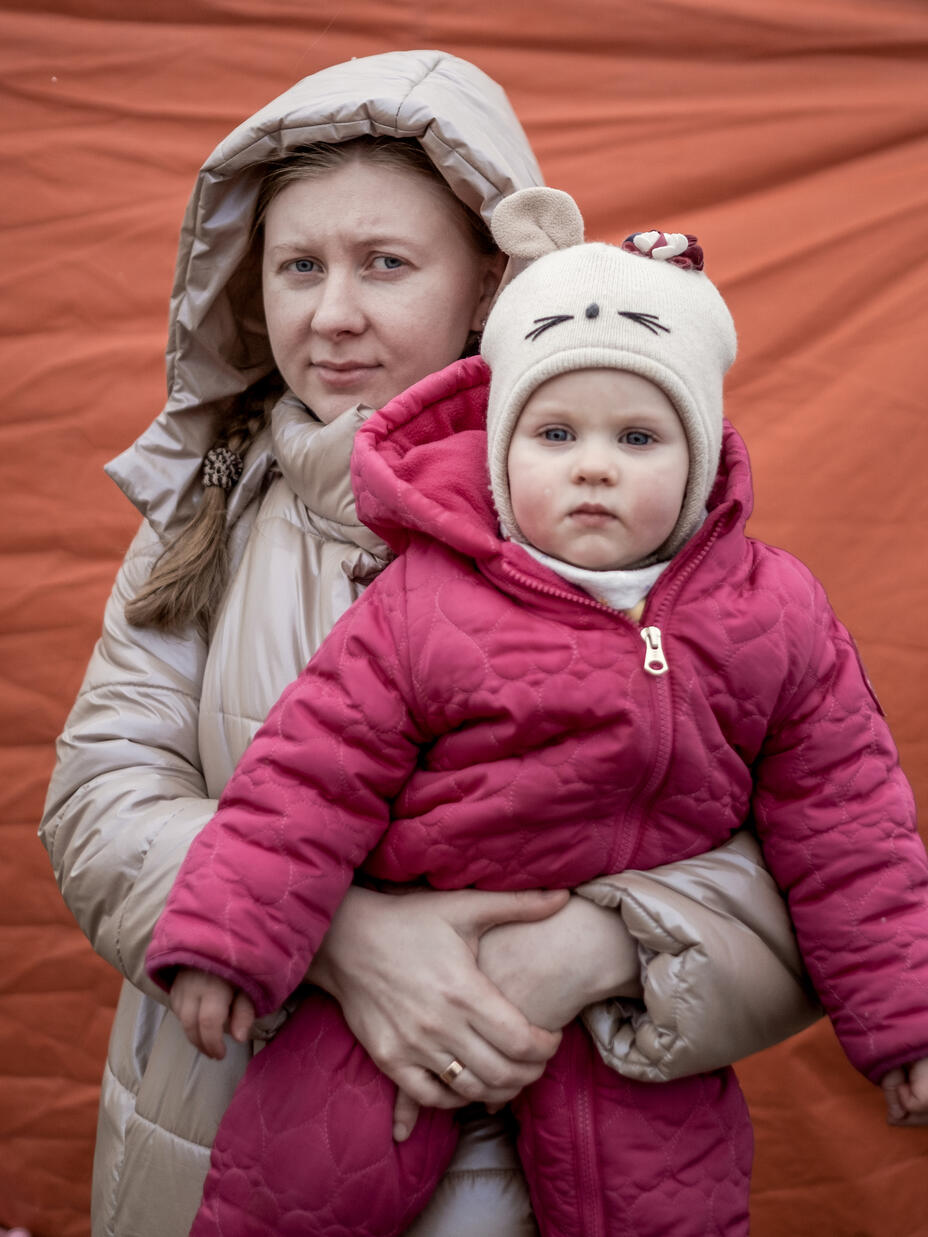 A woman holds a young girl, both in winter coats.