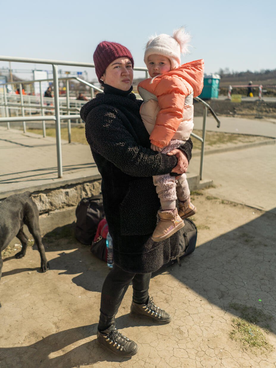한 여성이 겨울 코트와 모자를 쓴 딸을 안고 서 있습니다.