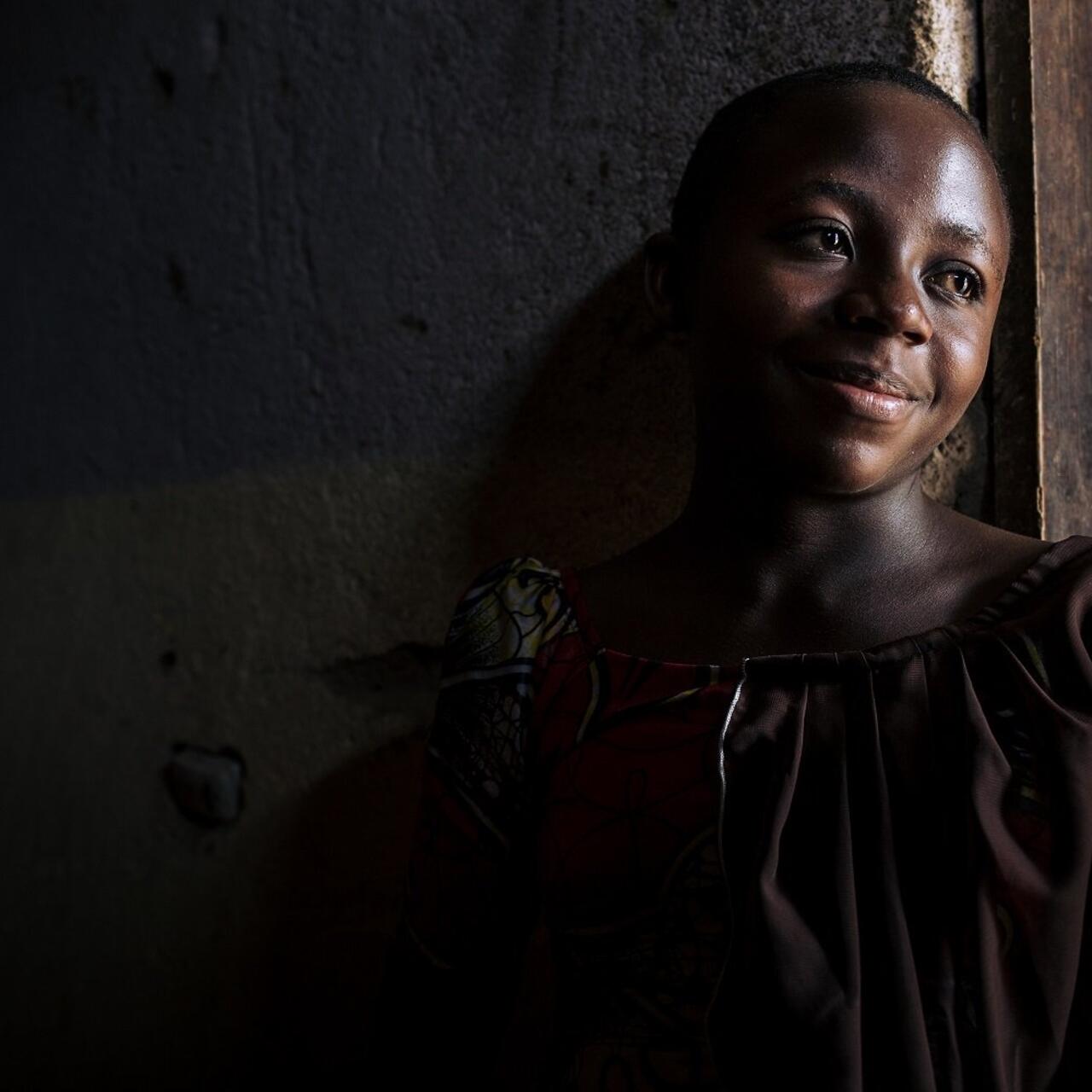A women is smiling and leaning against a wall