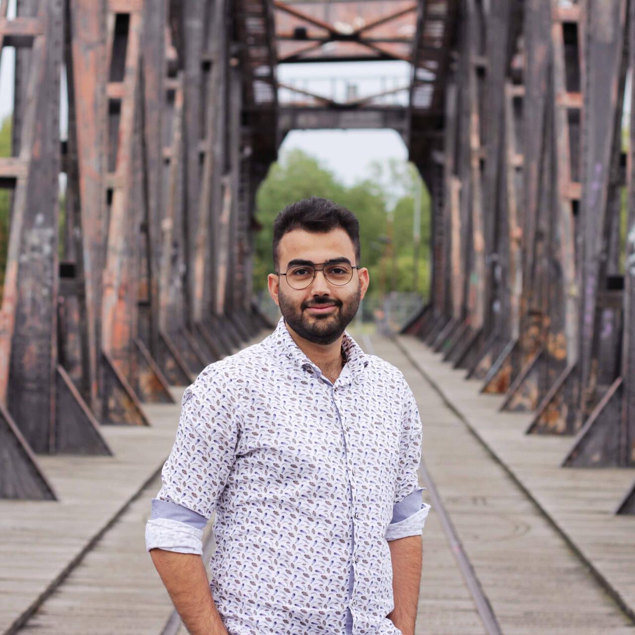 Zain, ein junger Mann steht auf einer Brücke in Magdeburg und lächelt in die Kamera.