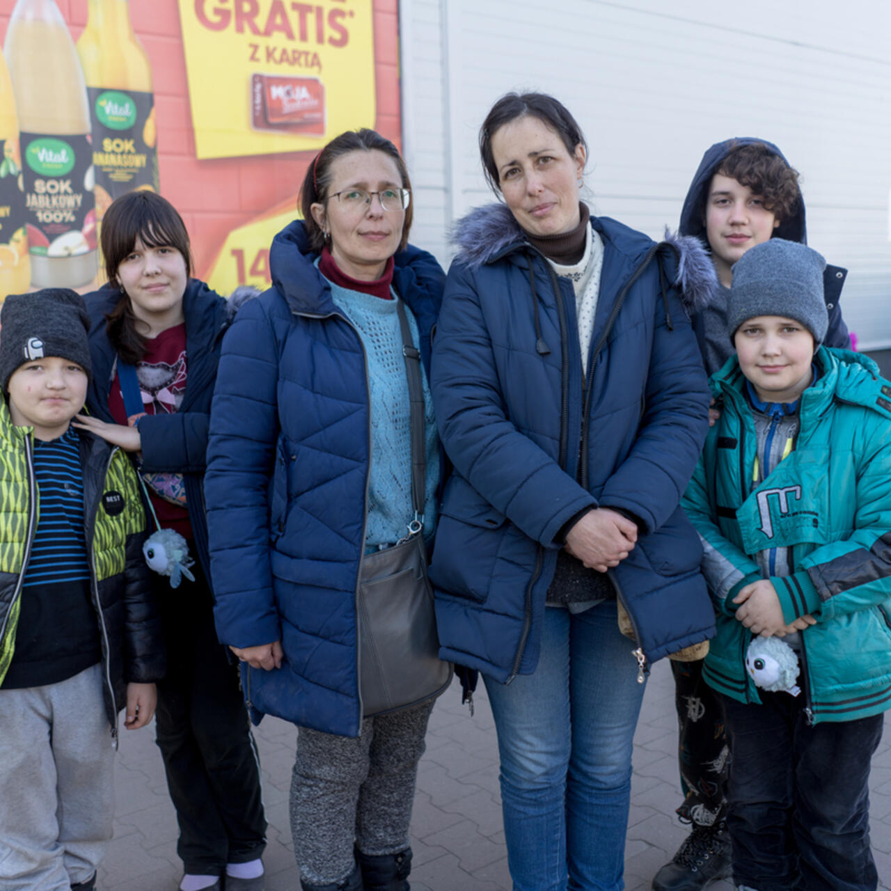 Two sisters stand together in a parklng lot. Each sister has her own two kids with her.