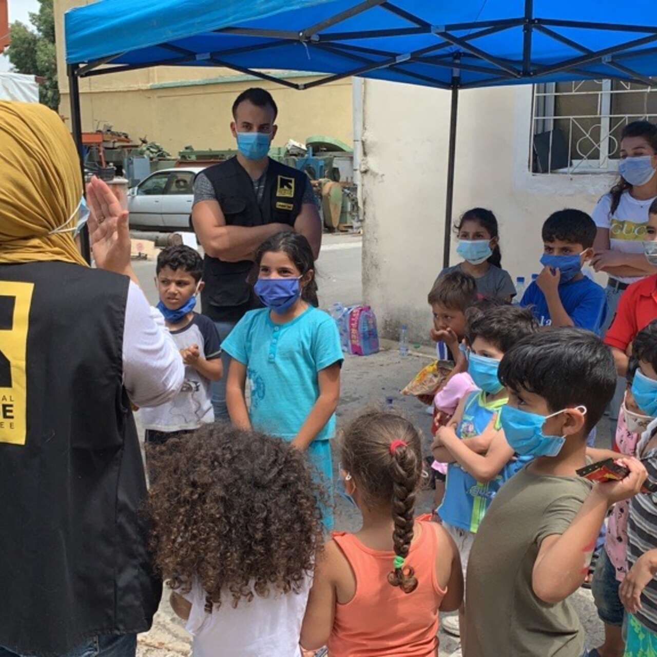 IRC staff members stand with a group of children and deliver psychosocial counseling. 