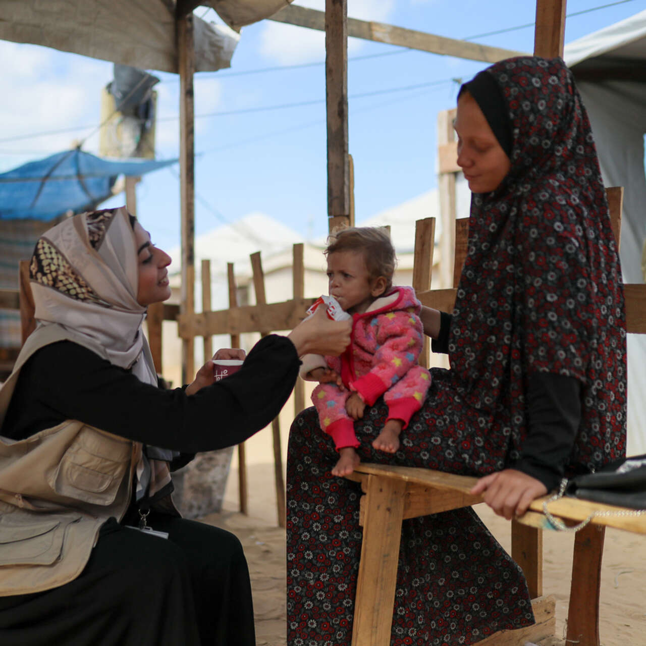 RESCUE:s medarbetare matar ett litet barn i Gaza med nötkräm mot undernäring. Barnet sitter i sin mammas knä.