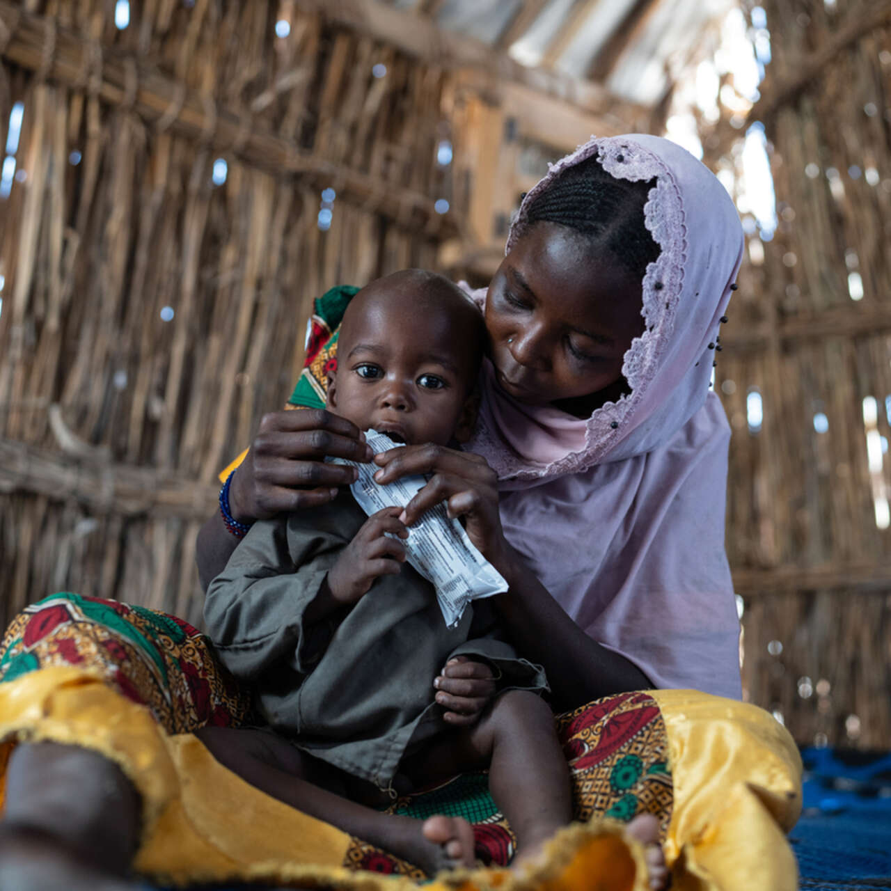 Ett litet barn i Tchad matas med nötkräm mot undernäring, han sitter i sin mammas famn. 