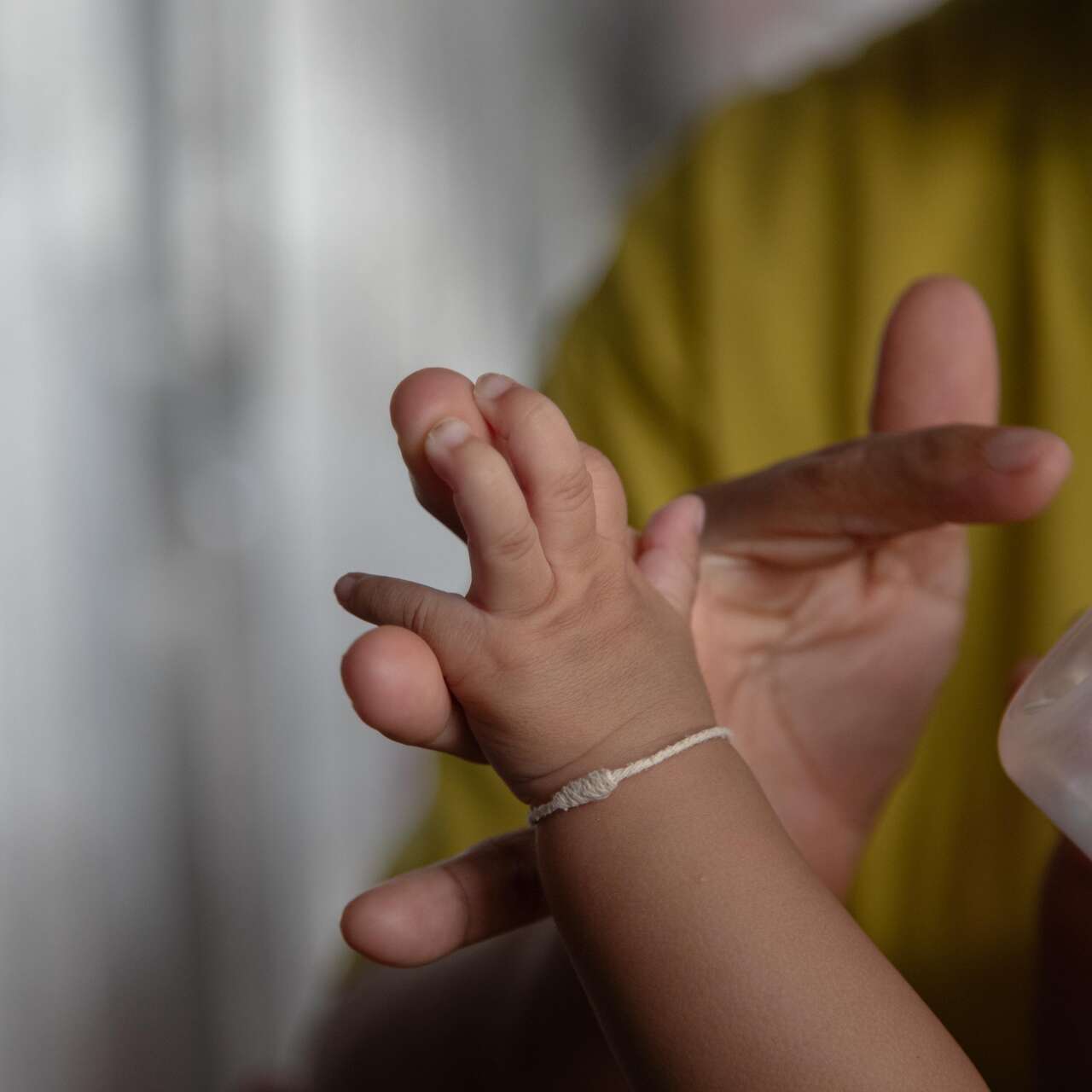 Nwe holds a baby bottle and her baby's hand.