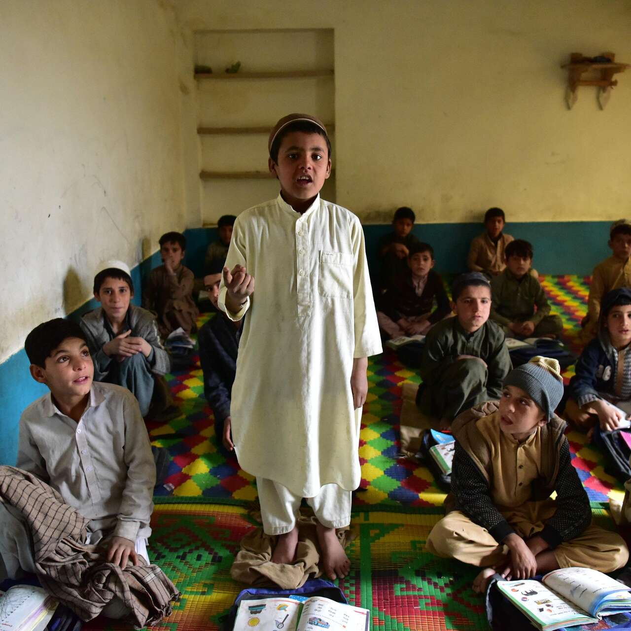 Children in a classroom, one of them is standing up and talking 