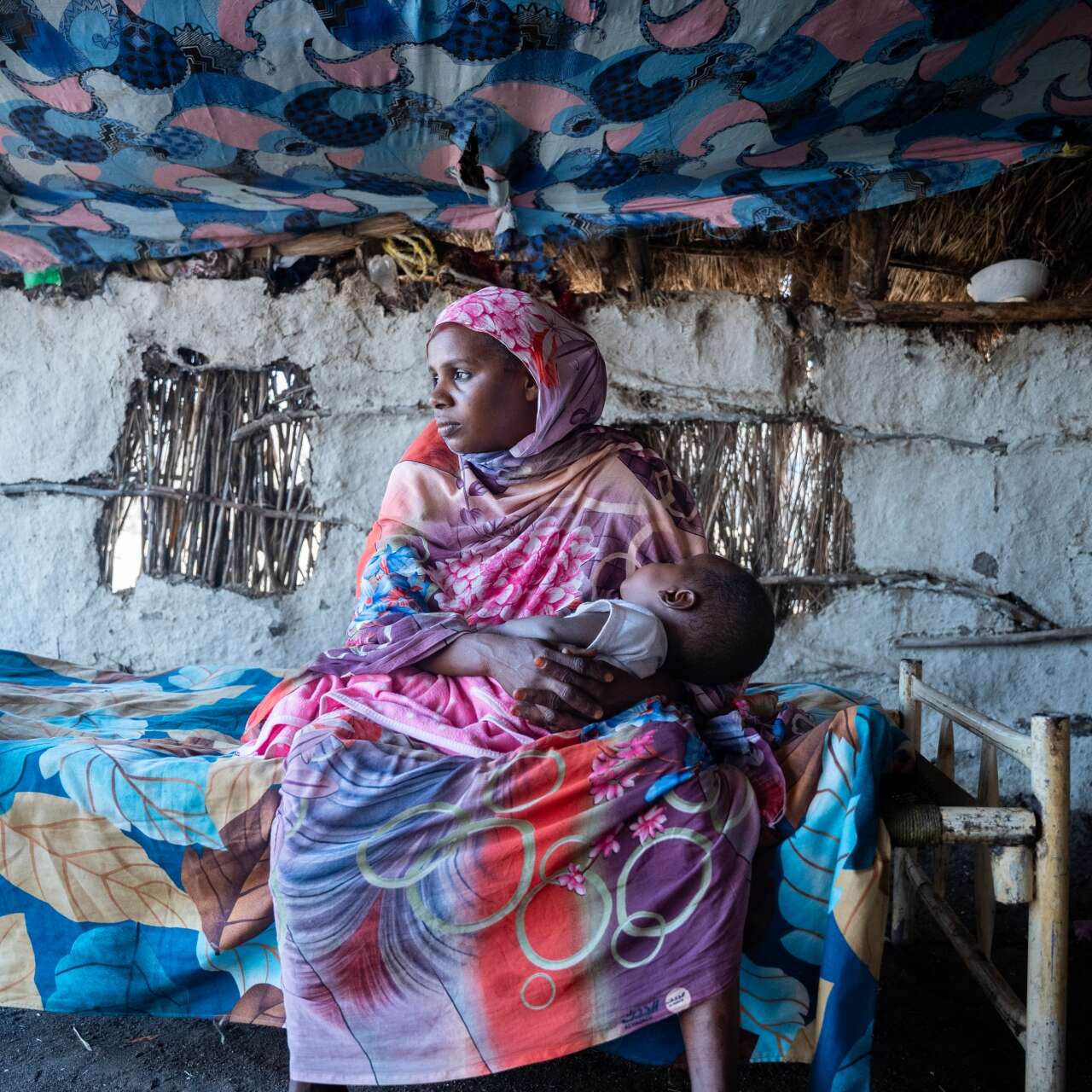 A mother holds her young child in her arms. The two are inside of a makeshift shelter in Sudan.