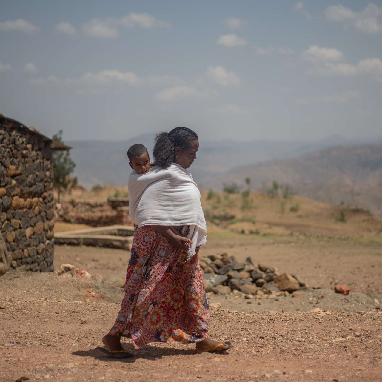 A mother walks through a barren Ethiopian landscape, carrying her young son on her back.