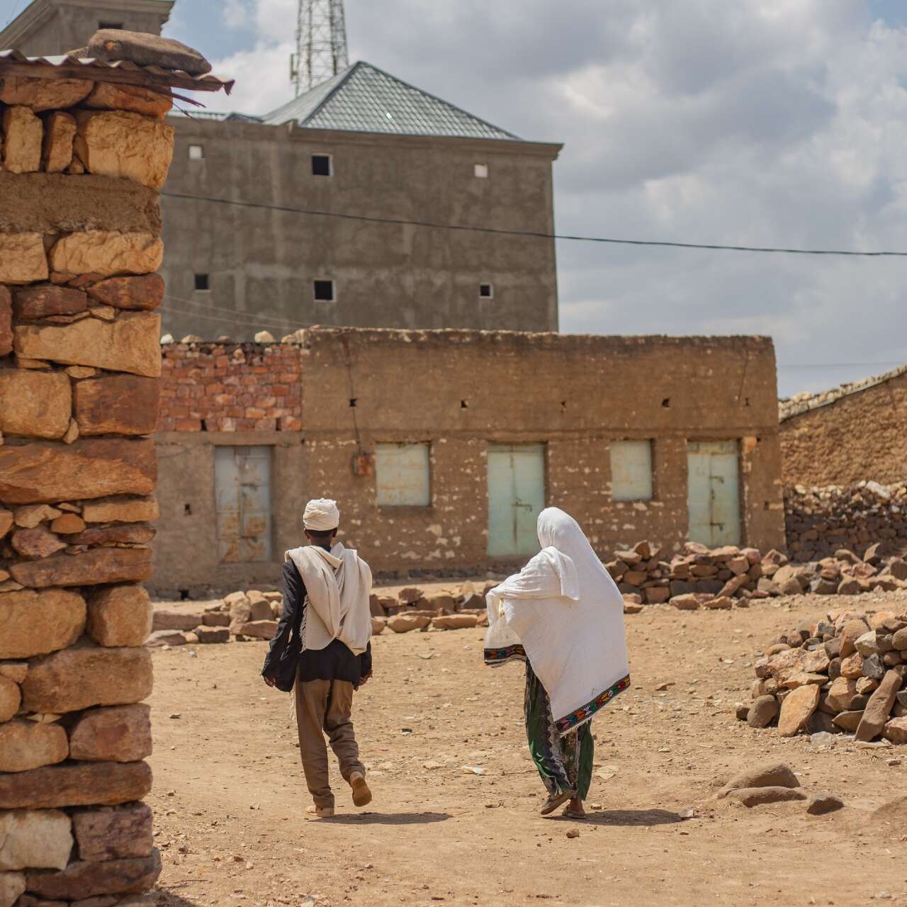 Two people walk through a rural Ethiopian village.
