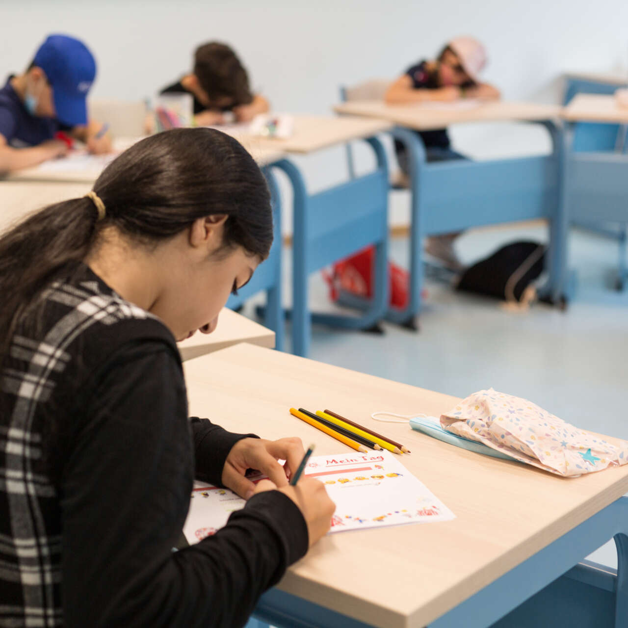 En flicka sitter vid en skolbänk och skriver. 