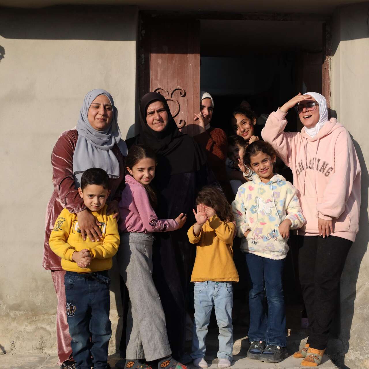 Al-Qusayr, Homs province, Syria. Bayan, 32, stands with her family at the entrance of their repaired family home after returning from 13 years of displacement in Lebanon.
