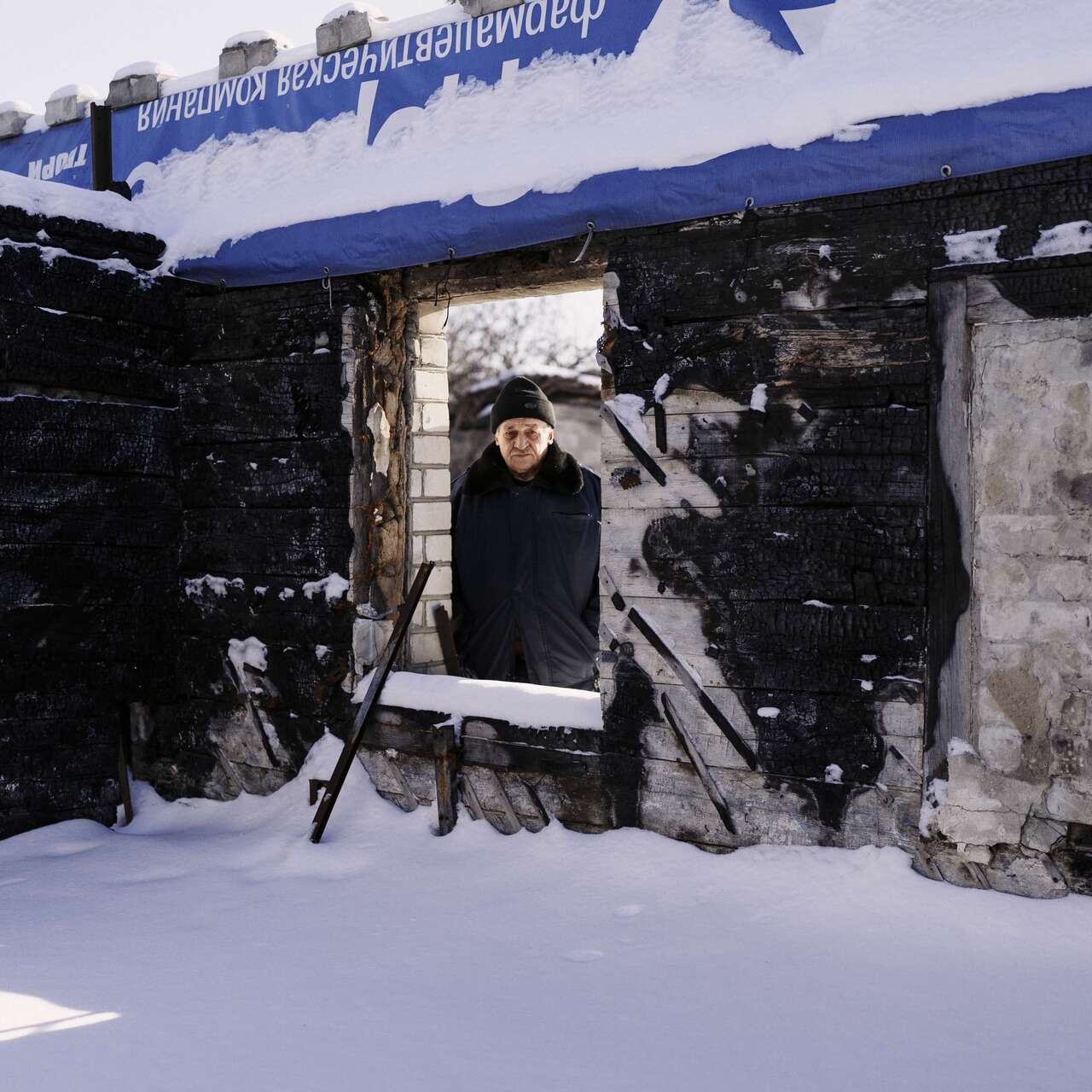 En man står och kollar igenom ett fönster för ett nedbrunnet hus.